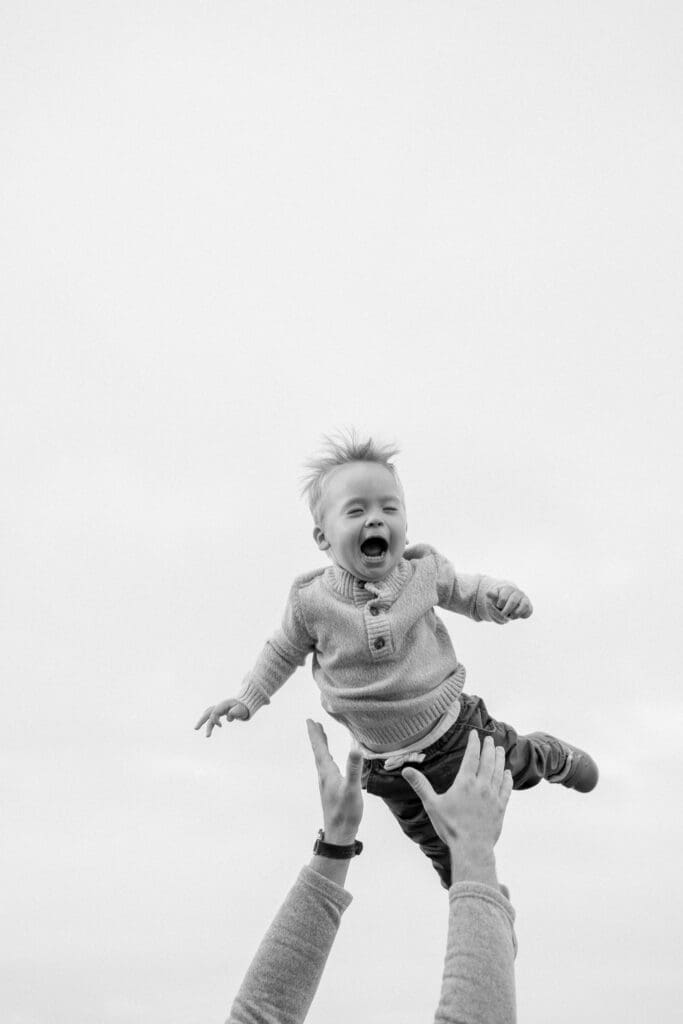 A black and white photo of a little boy laughing while being tossed in the air by his dad.