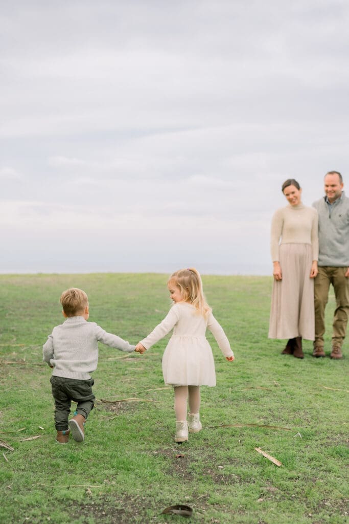 A little boy and girl hold hands and walk towards their mom and dad.