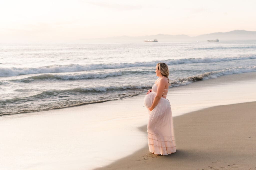 A beautiful sunset photo of a pregnant woman on the beach holding her belly.
