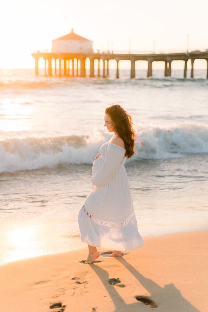 If you are wondering what to wear for maternity photos in Los Angeles, this woman is in a long white dress on the beach.