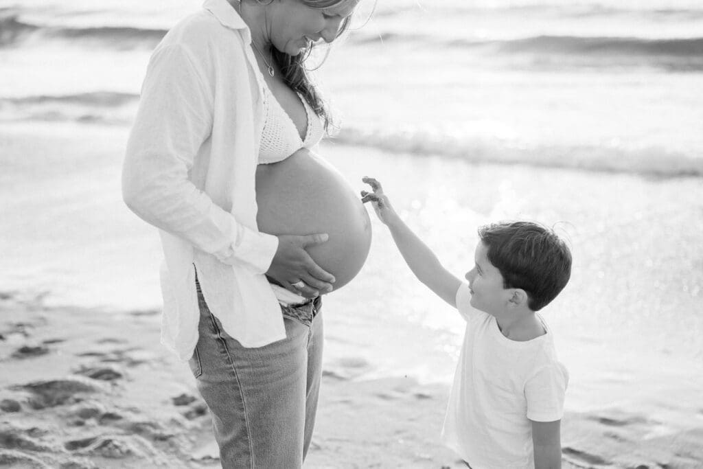 A little boy in jeans and a white t-shirt touches his pregnant mom's belly during their maternity photos in Los Angeles.