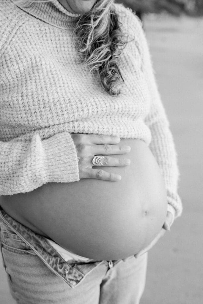 A close up photo of a pregnant belly while the mom is wearing jeans and sweater.