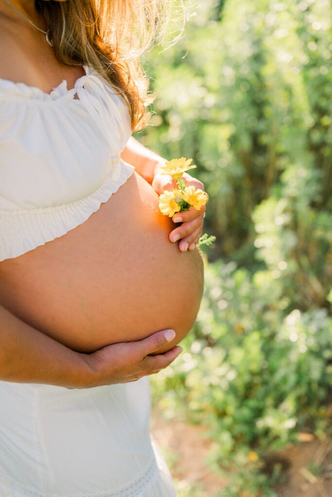 A close up photo of a pregnant belly with yellow flowers next to it.