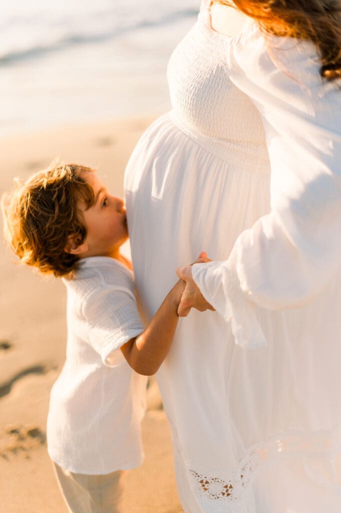 A little boy kisses his mom's pregnant belly as they pose for maternity photos.