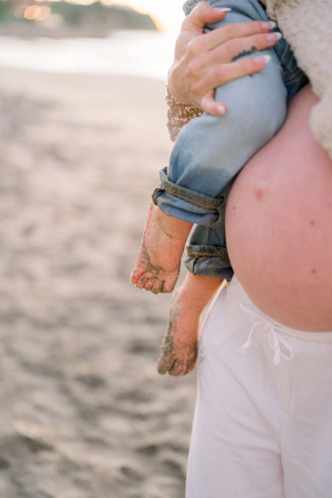 A photo of a pregnant mom holding her young son at the beach.