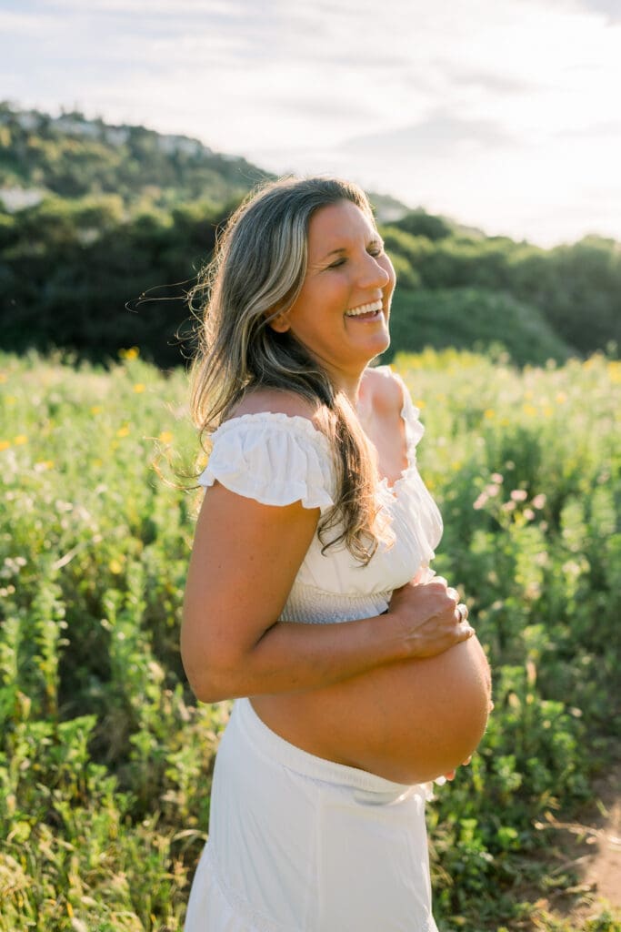 A pregnant mom laughs and holds her belly during her Los Angeles maternity session.