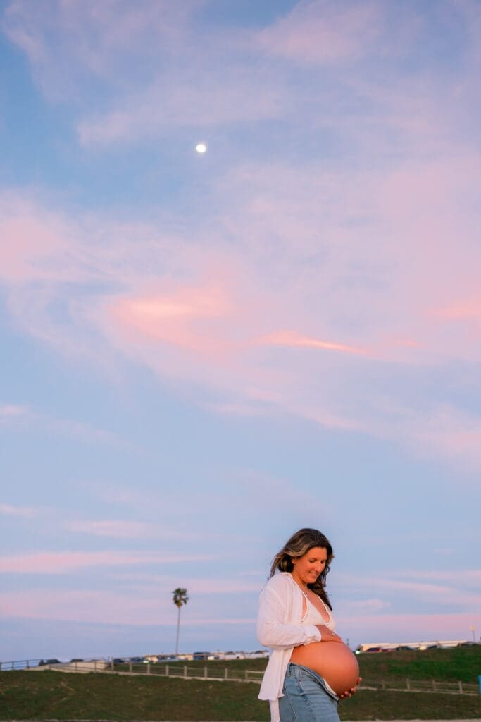 A photo of a pregnant mom under the moon with a beautiful blue and pink sky.