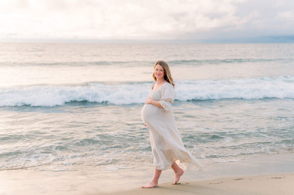 A pregnant woman walking on the beach during her Los Angeles maternity session at the beach.