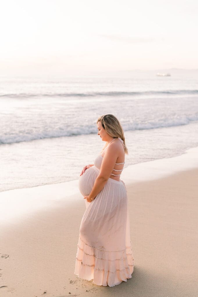 A pregnant mom holding her belly on the beach during her Los Angeles maternity session.