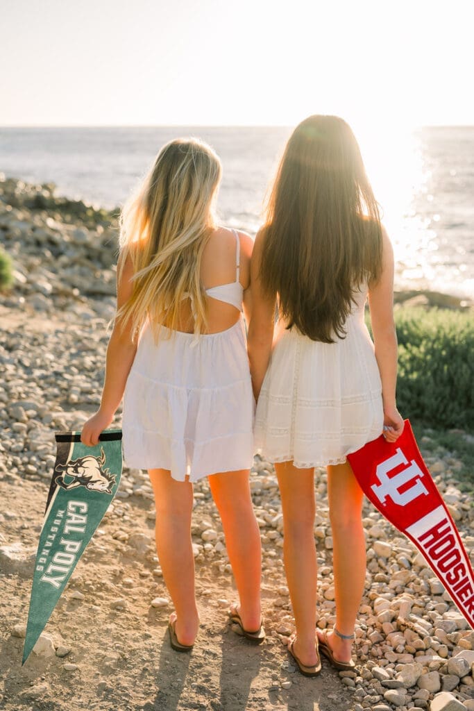 Girl friends holding their college banners and posing for Los Angeles senior photos at the beach.