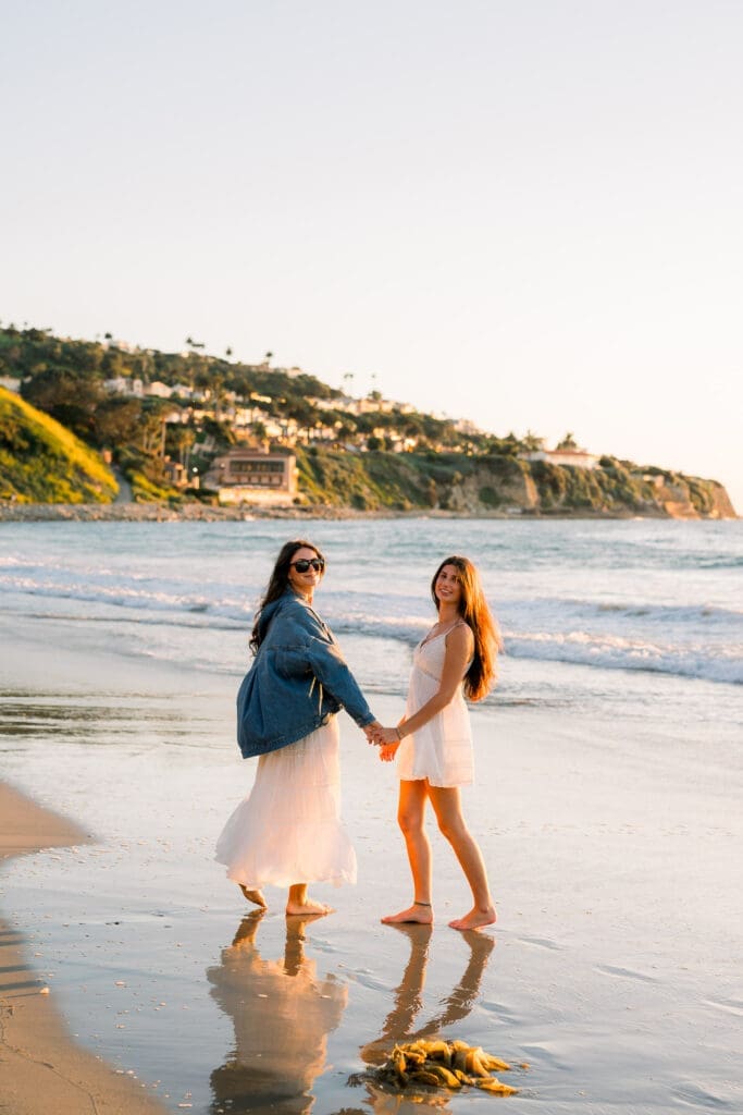 A mom and daughter walking on the beach at sunset while taking senior photos.