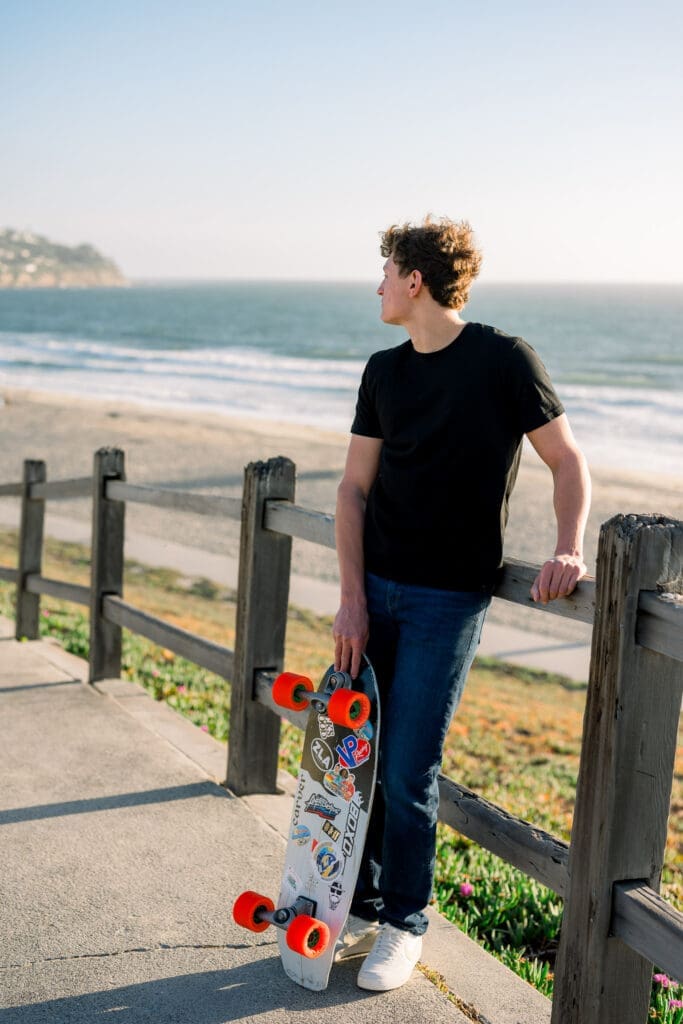 A boy standing at the beach with his skateboard posing for Los Angeles senior photos.