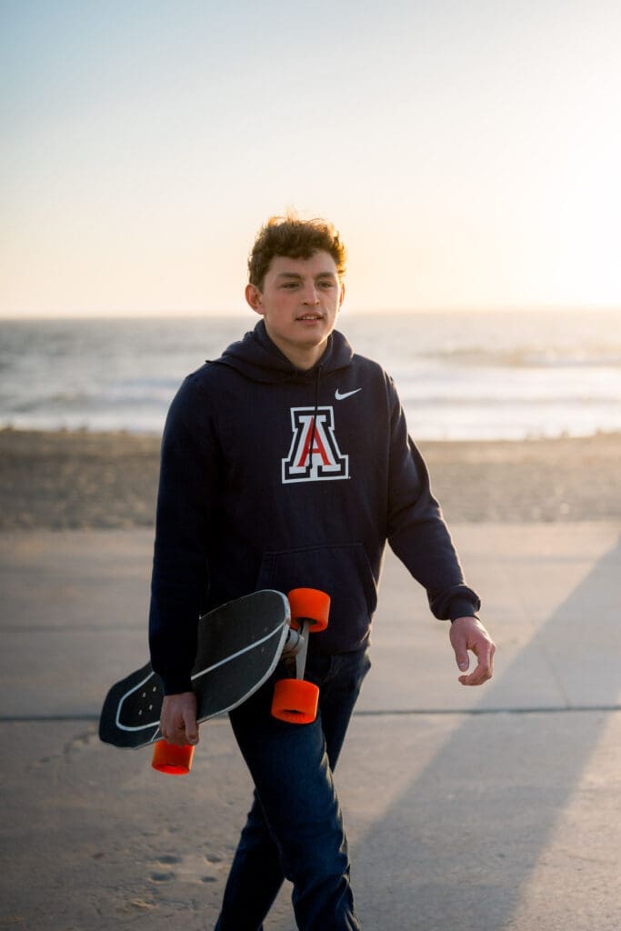 A Los Angeles senior photo session featuring a boy in a college sweatshirt holding his skateboard.