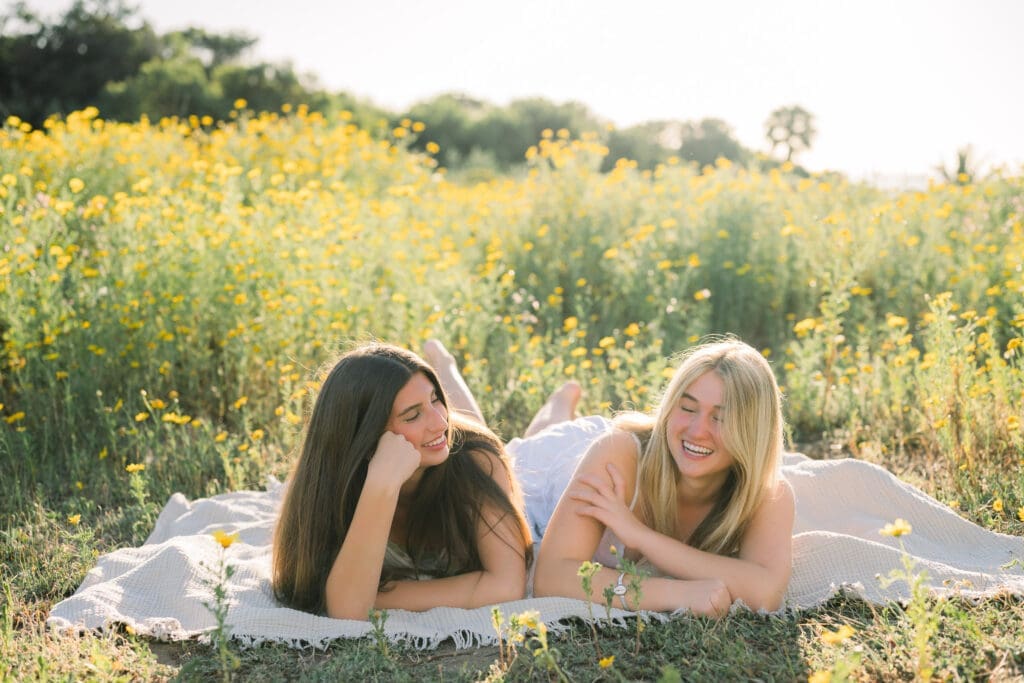 Two young girls laughing in a field of wildflowers during their Los Angeles senior photo session.