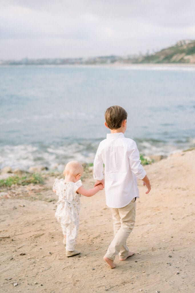 Siblings holding hands and walking on the beach while taking spring family portraits in Los Angeles.