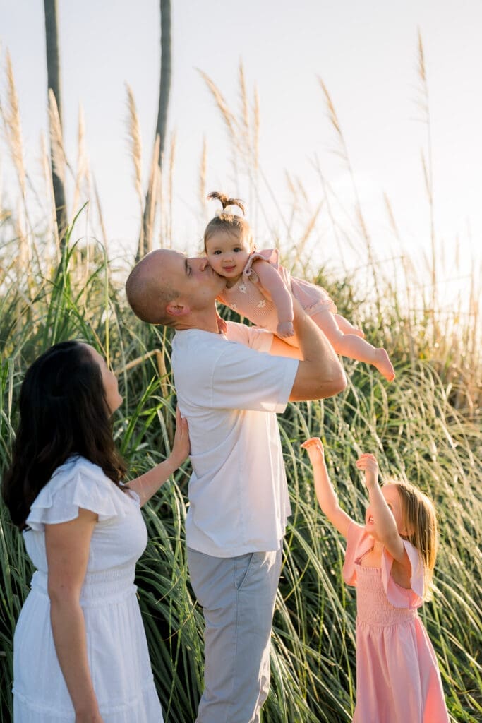 A dad kisses his daughter's cheek while his wife and other daughter look on lovingly.