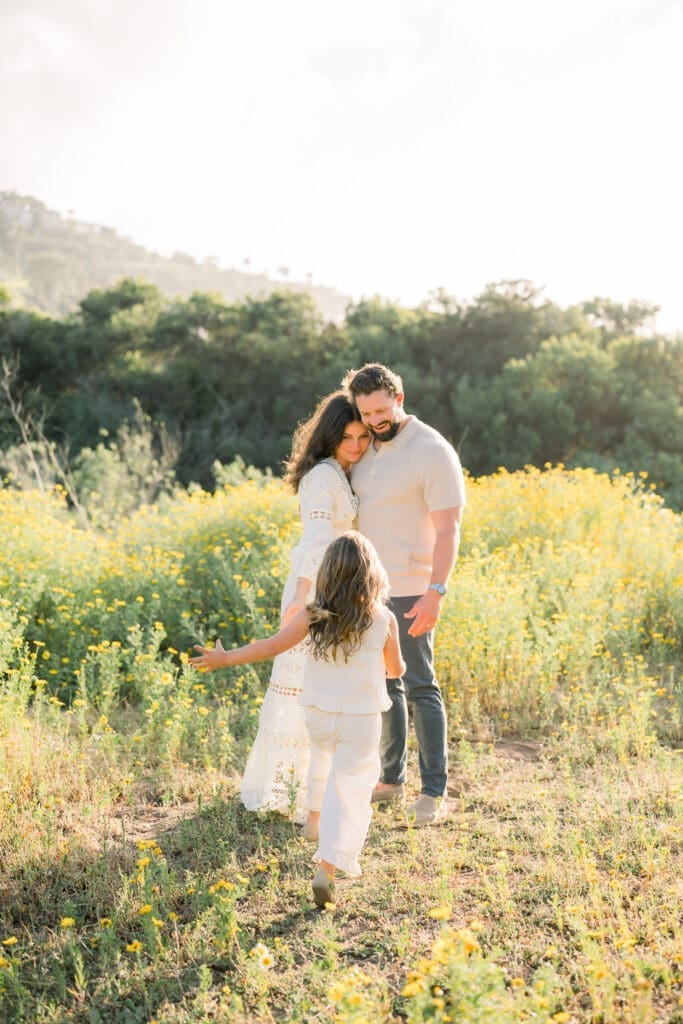 A little girl running towards her parents at sunset among the wildflowers.