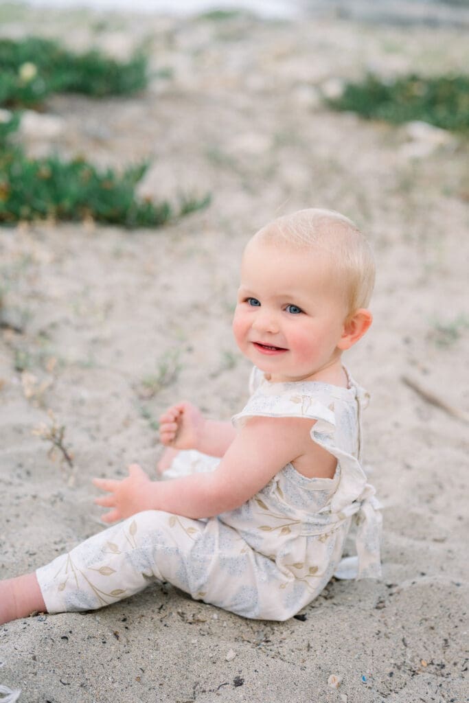 A little girl sitting on the beach in the sand.