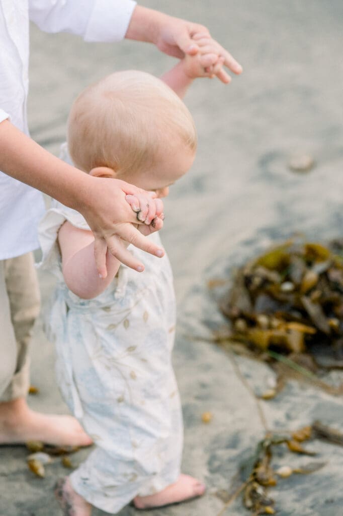 A little girl holding her brother's hands and walking on the beach.