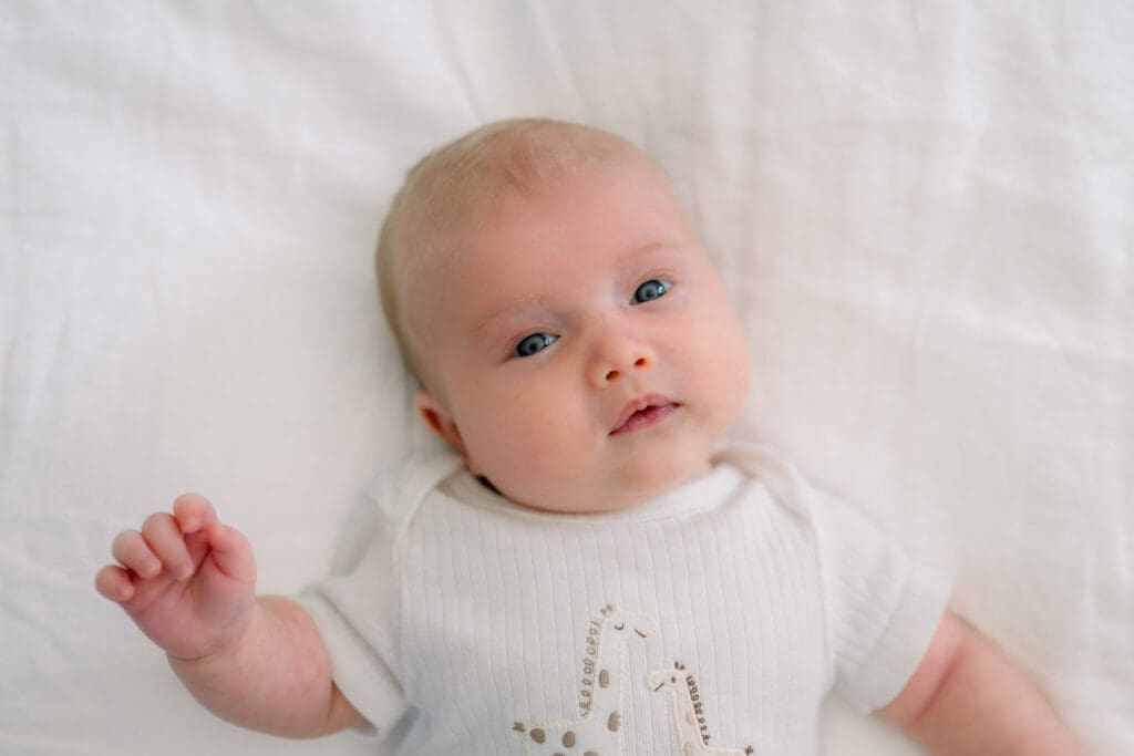 An example of what to wear for newborn photos at home showing a baby in a neutral colored onesie.