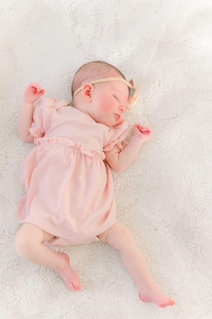 A newborn baby girl in a pink dress sleeps peacefully during her in home newborn session.