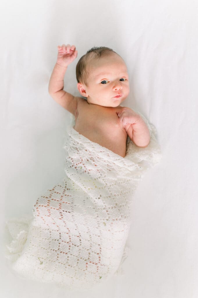 A baby wrapped in a white blanket taking newborn photos at home.