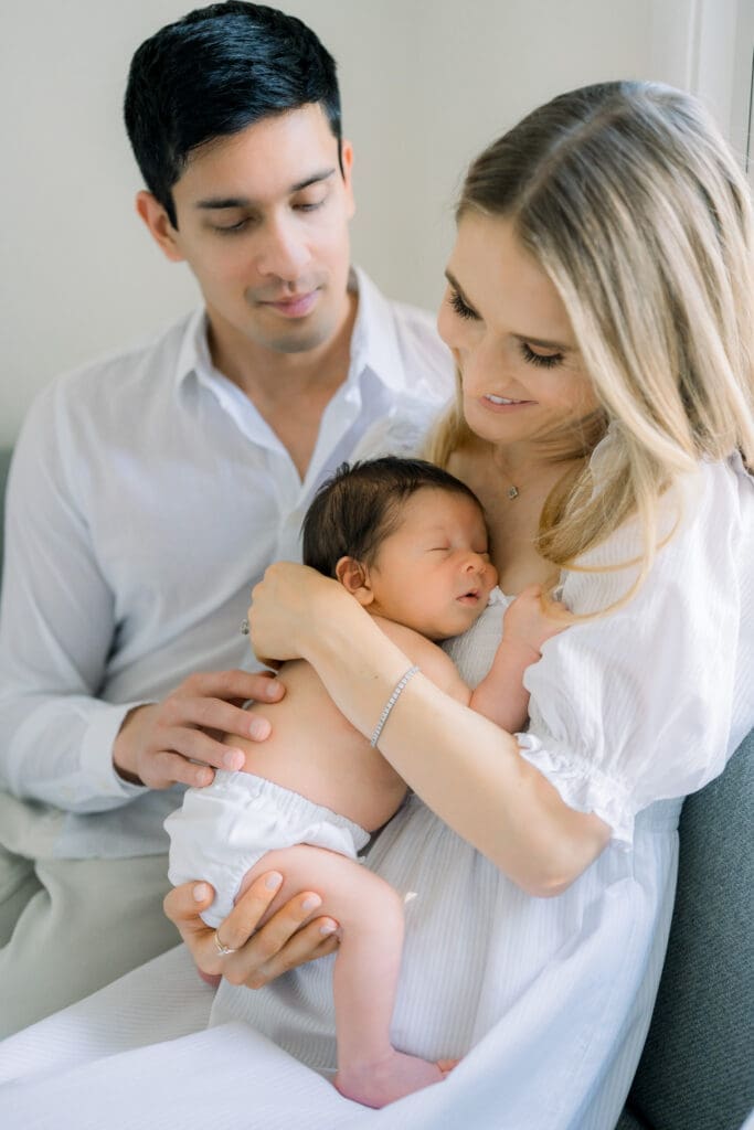 A mom and dad holding their newborn baby wearing white bloomers for his in home newborn session.