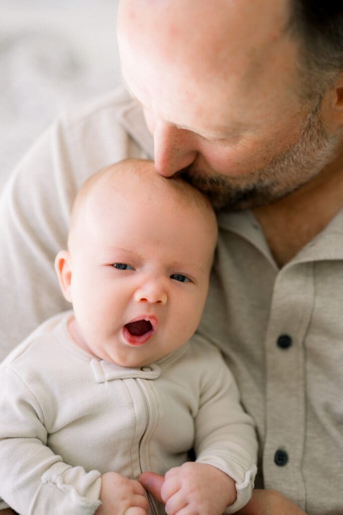 A dad and baby wearing neutral colored clothing for their newborn photos at home.