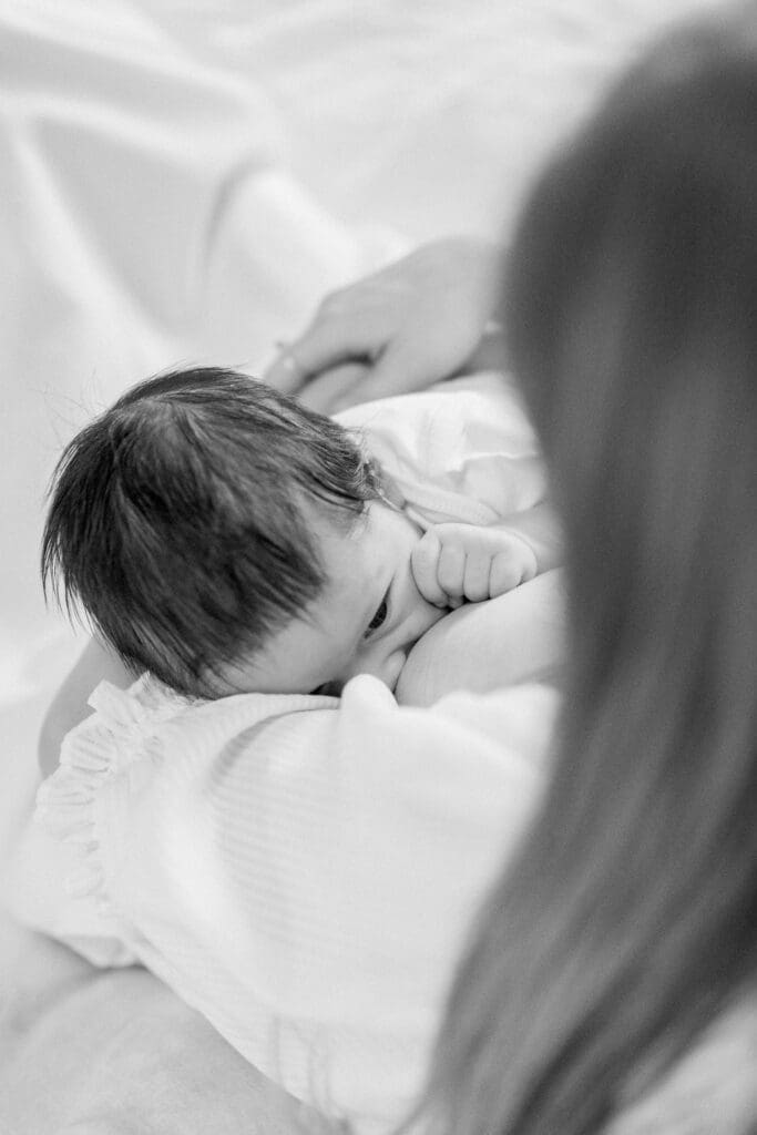 A black and white photo of a newborn baby nursing during a newborn photo session at home.