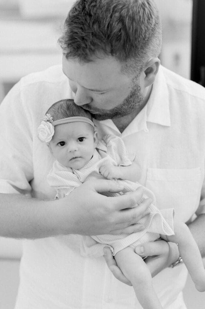 A dad kissing his newborn baby during a newborn photo session at home.