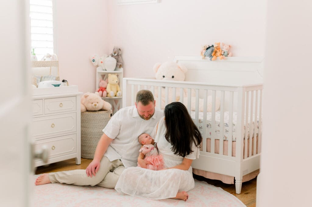 A family sitting on the floor of their nursery holding their newborn baby.