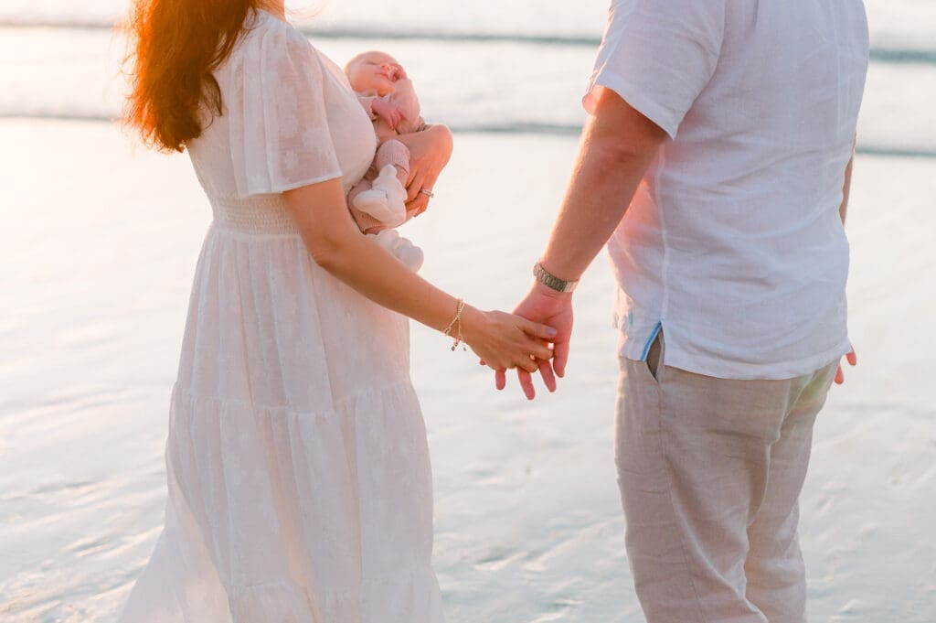 A family taking outdoor newborn photos on a beach at sunset.