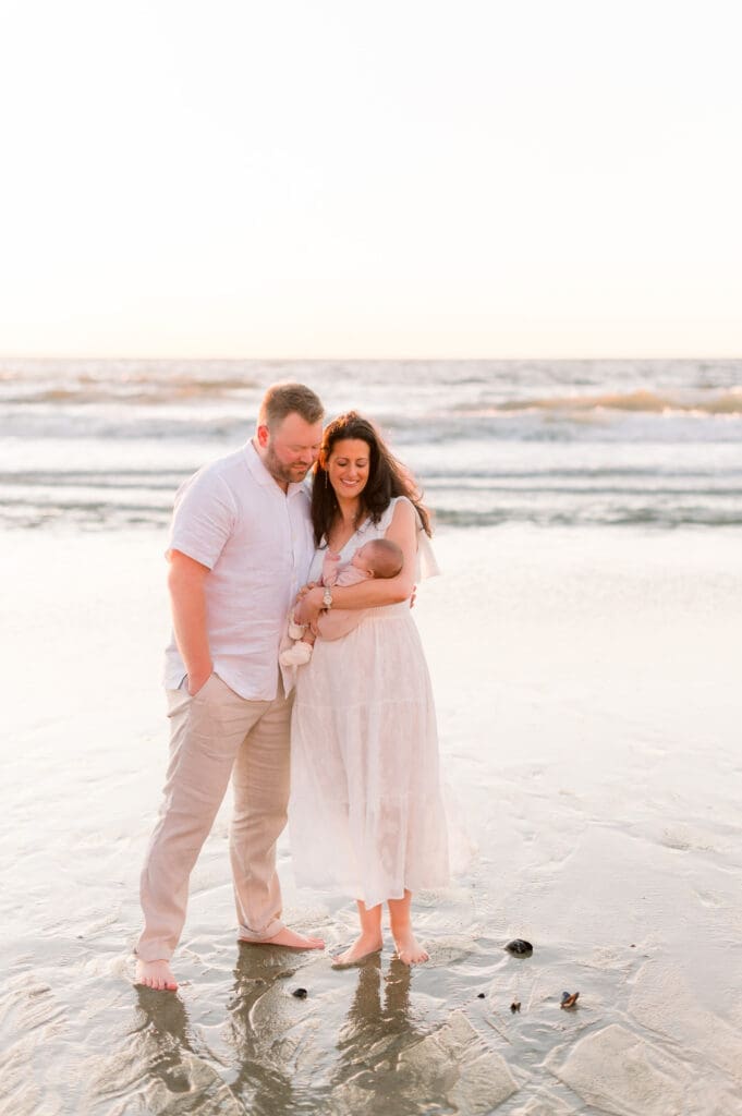 Mom and dad holding their new baby at the beach while taking outdoor newborn photos.