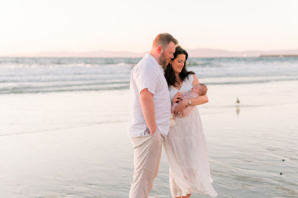 Outdoor newborn photos taken at the beach at sunset where mom and dad hold their newborn baby.