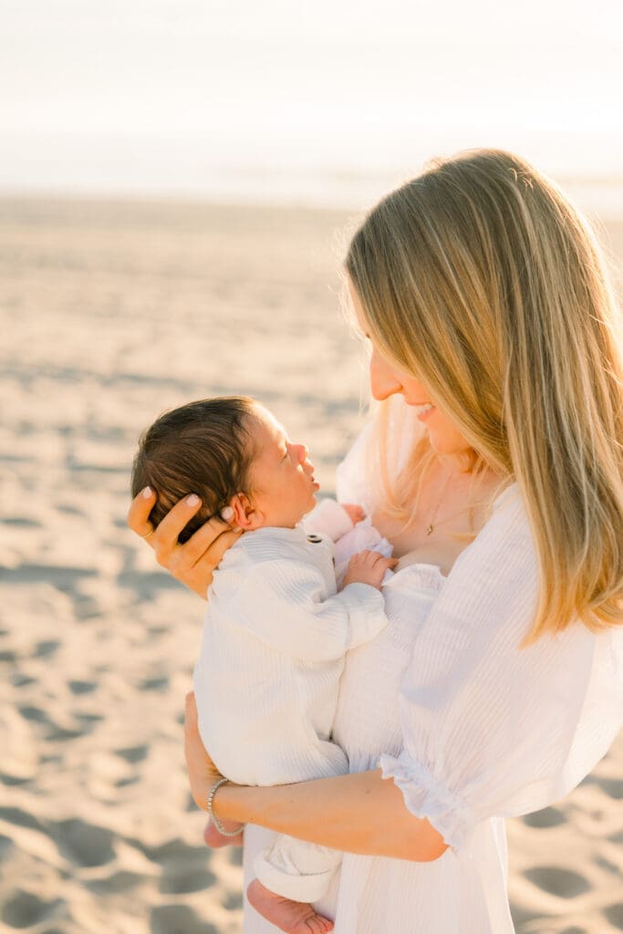 A mom snuggles her newborn baby while taking outdoor newborn photos on the beach.