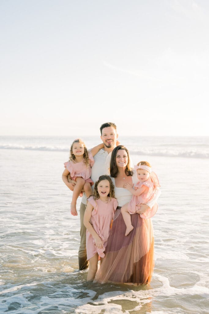 A family of 5 poses on the beach for family photos.