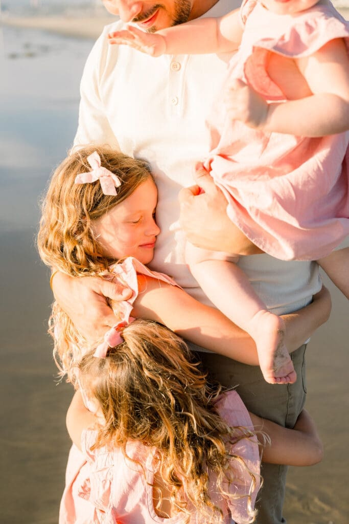 A girl in a pink dress hugs her dad while taking photos at a family mini session in Manhattan Beach.
