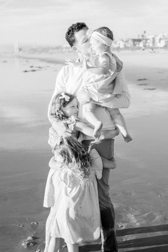 Dad and his girls hugging on the beach.