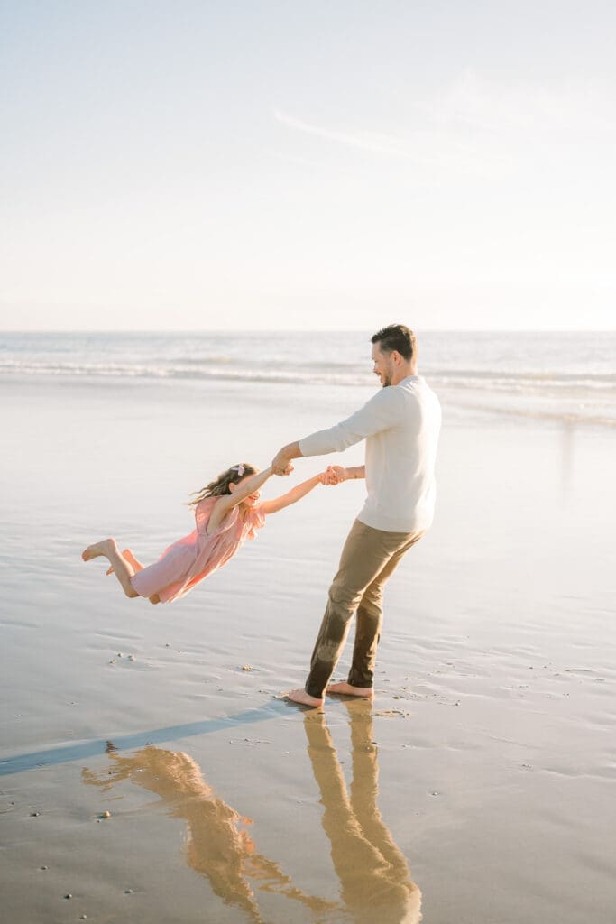 Dad swinging his daughter around on the beach in the South Bay while taking family photos.