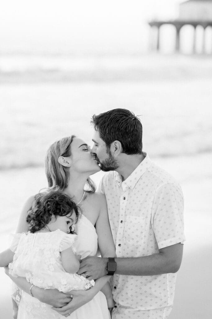 A couple kissing on the beach while posing for family photos.