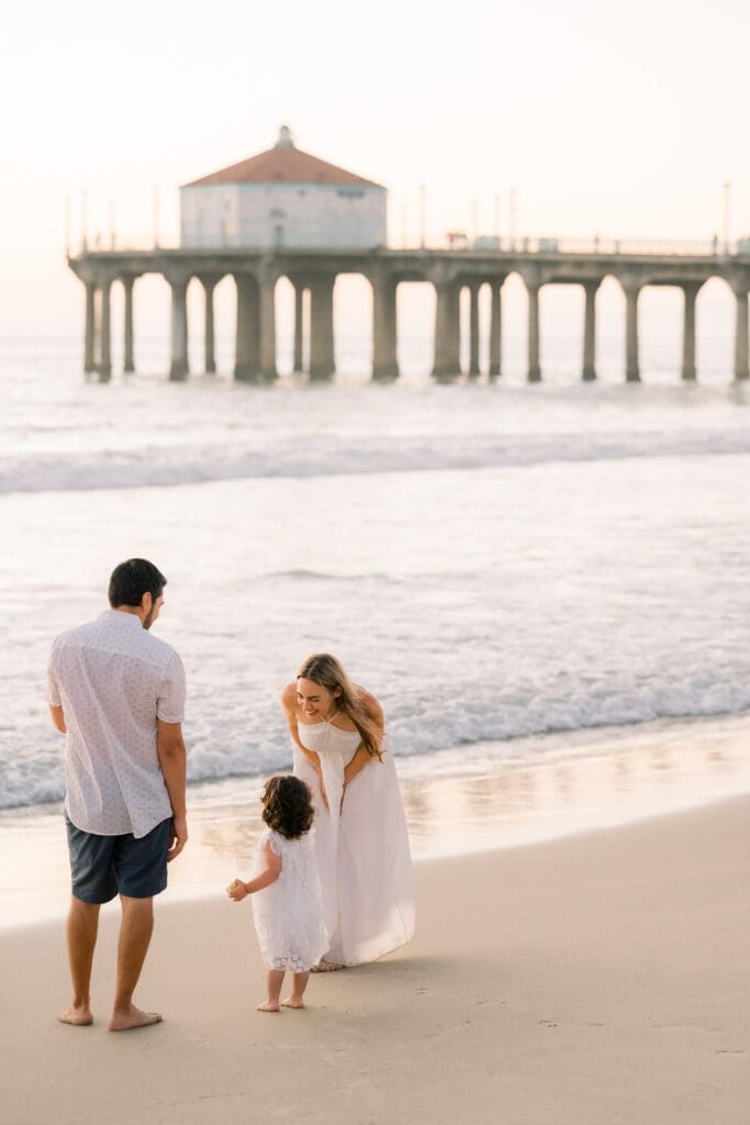 A family playing on the beach with the Manhattan Beach pier in the background.