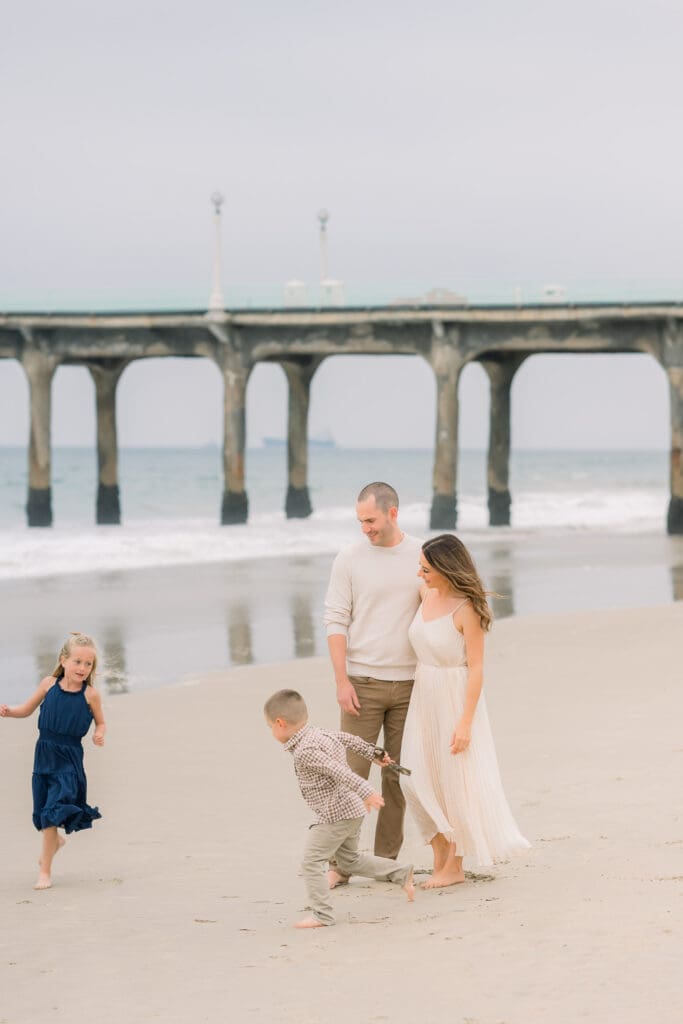 A family playing on the beach by the Manhattan Beach pier during their family photo session.