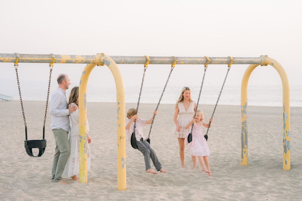 A family swinging on a swing set in Hermosa Beach, which is one of the best South Bay family photo locations.