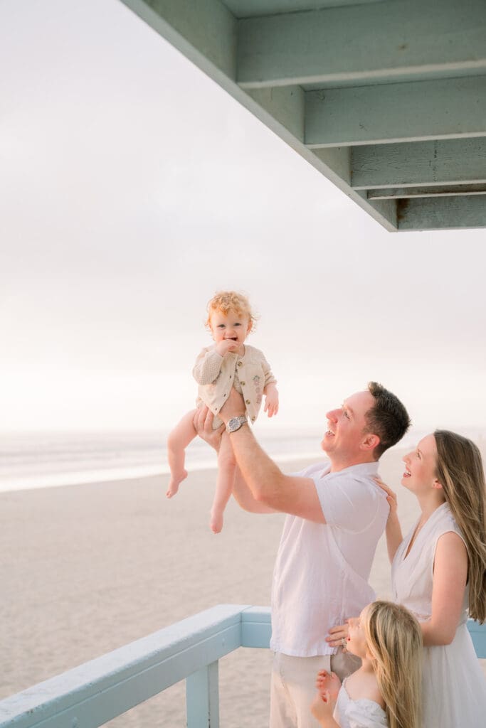 A family holding up their littlest baby on a lifeguard tower in Manhattan Beach.
