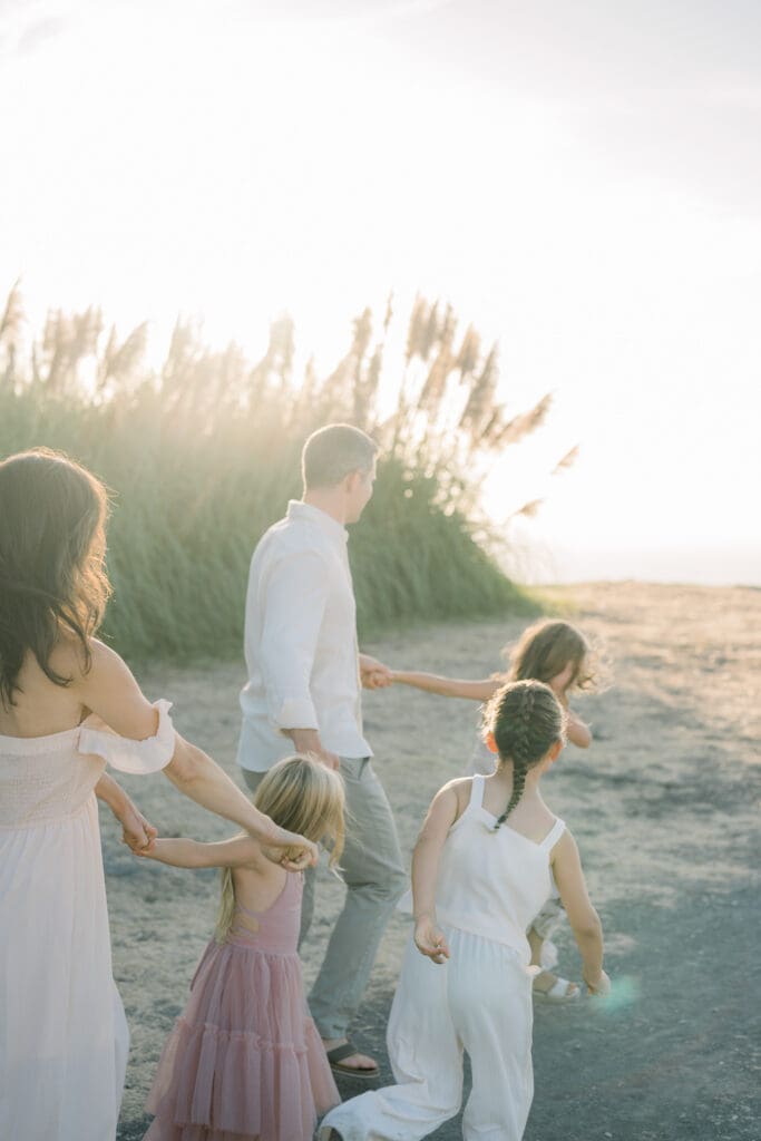 A family holding hands and walking along the pampas grass of the Palos Verdes Cliffs at sunset.