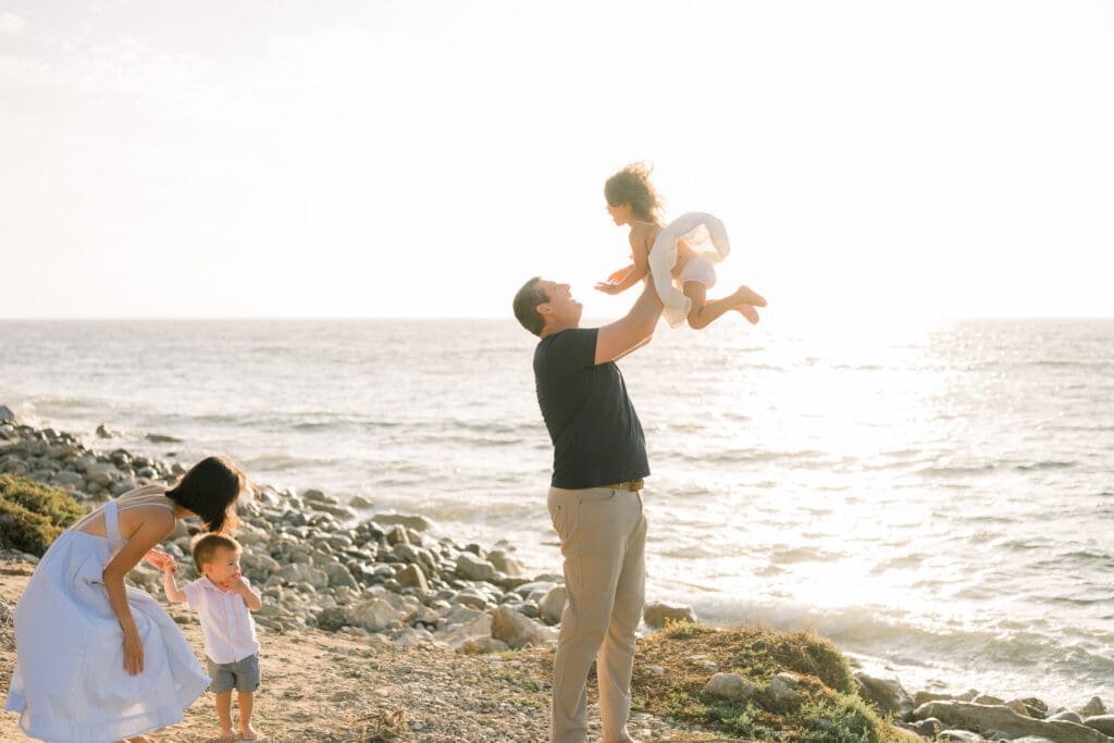 Dad throwing his daughter up in the air by the beach at sunset.