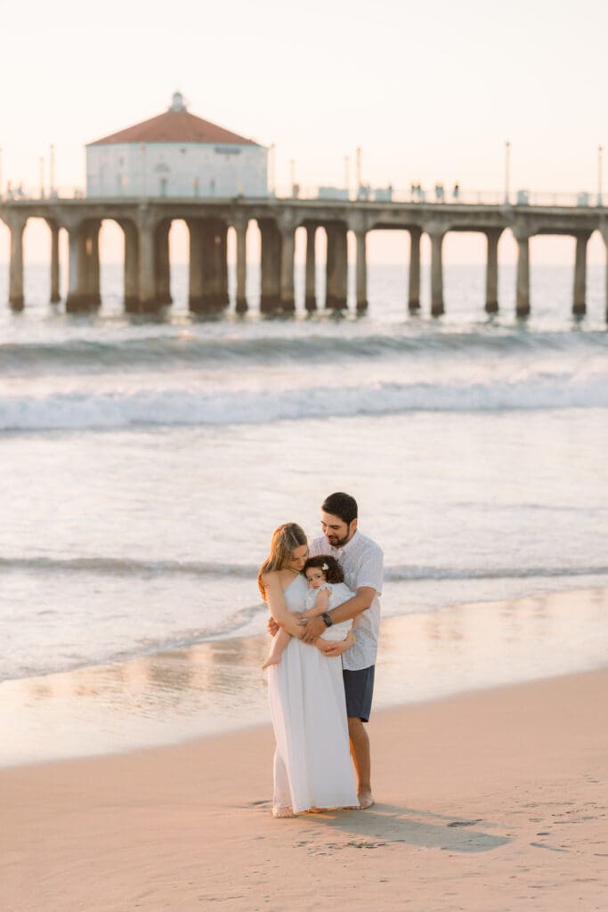 A family posing for photos with the Manhattan Beach pier in the background.