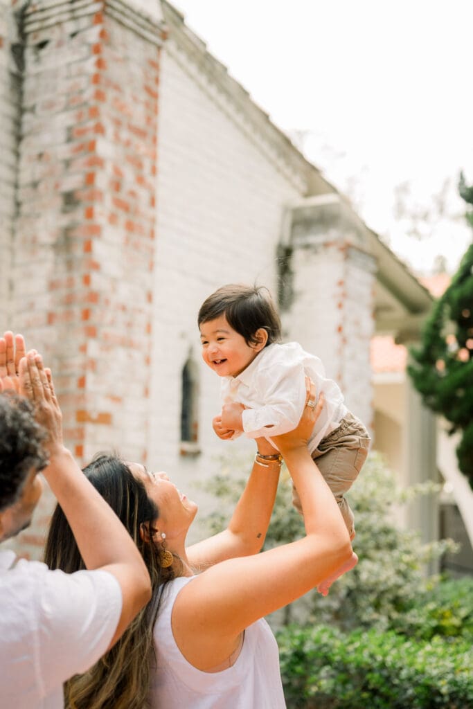 A mom holding her son up in the air while dad plays.